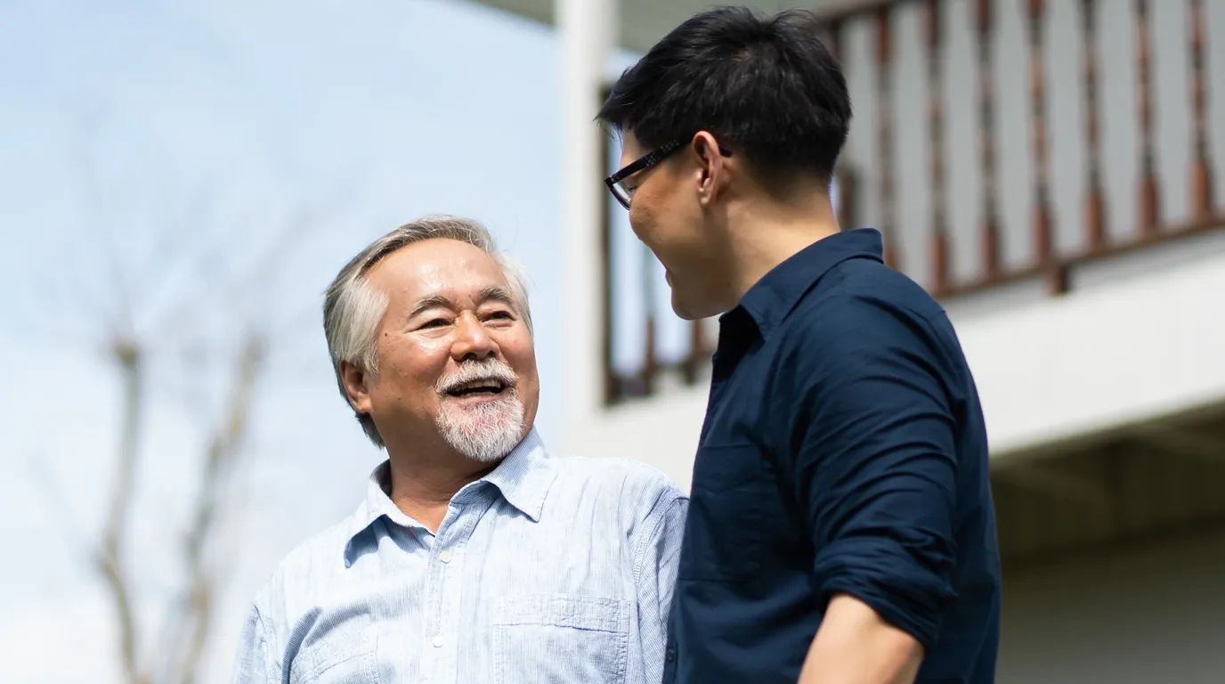 An older man and his adult son sharing a warm conversation outdoors in natural light — the kind of moment a clinical study journey supports.